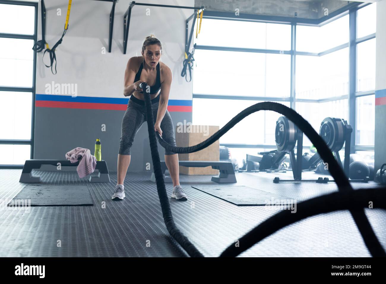 Kaukasische fit Frau, die im Fitnessstudio mit Kampfseilen trainiert Stockfoto