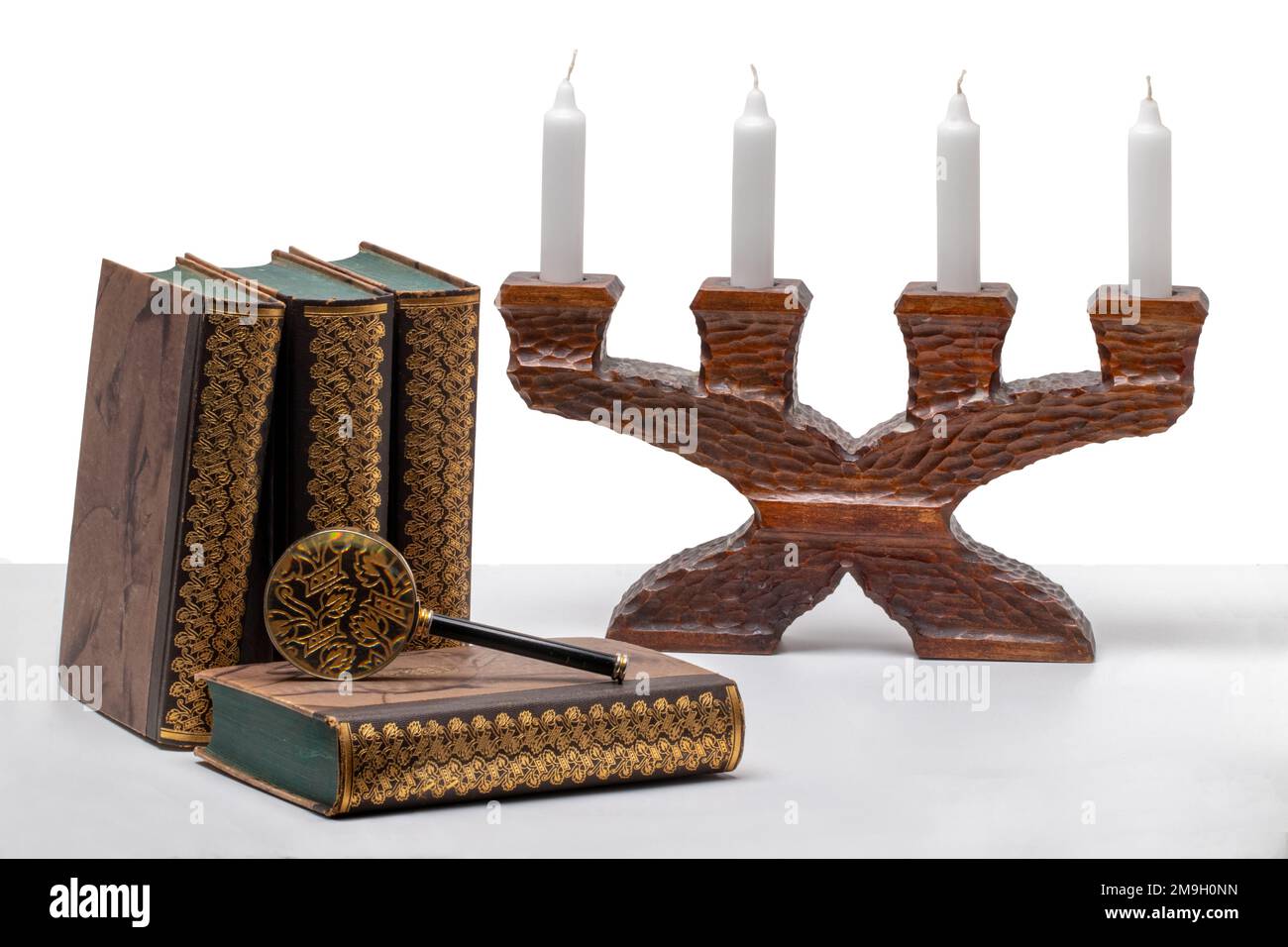 Alte Bücher mit einer Lupe und einem antiken Kerzenhalter aus Holz auf einem hellen Tisch isoliert auf weißem Hintergrund. Stockfoto