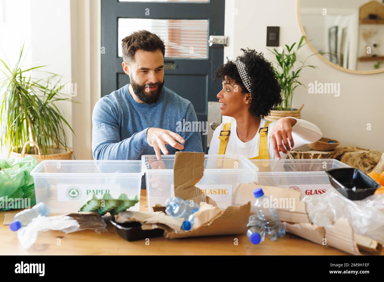 Birassisches junges Paar, das Papier, Kunststoffe und Gläser in Mülltonnen auf dem Tisch diskutiert und sortiert Stockfoto