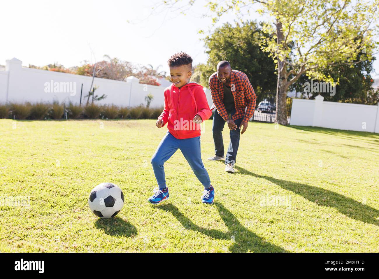 Glücklicher afroamerikanischer Vater und Sohn, die im Garten Fußball spielen Stockfoto