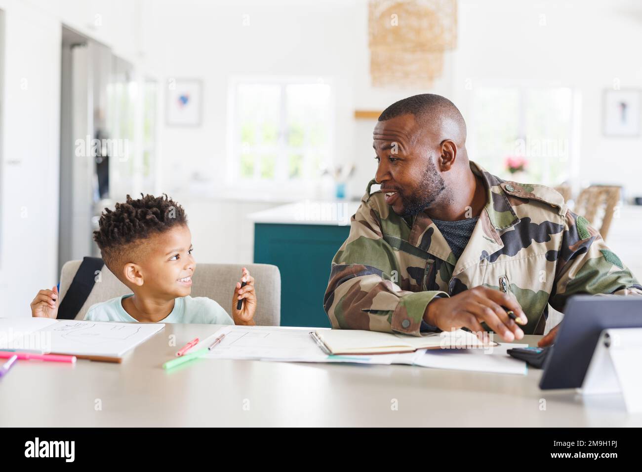 Glücklicher afroamerikanischer Vater in Militäruniform und sein Sohn arbeitet und macht Hausaufgaben Stockfoto
