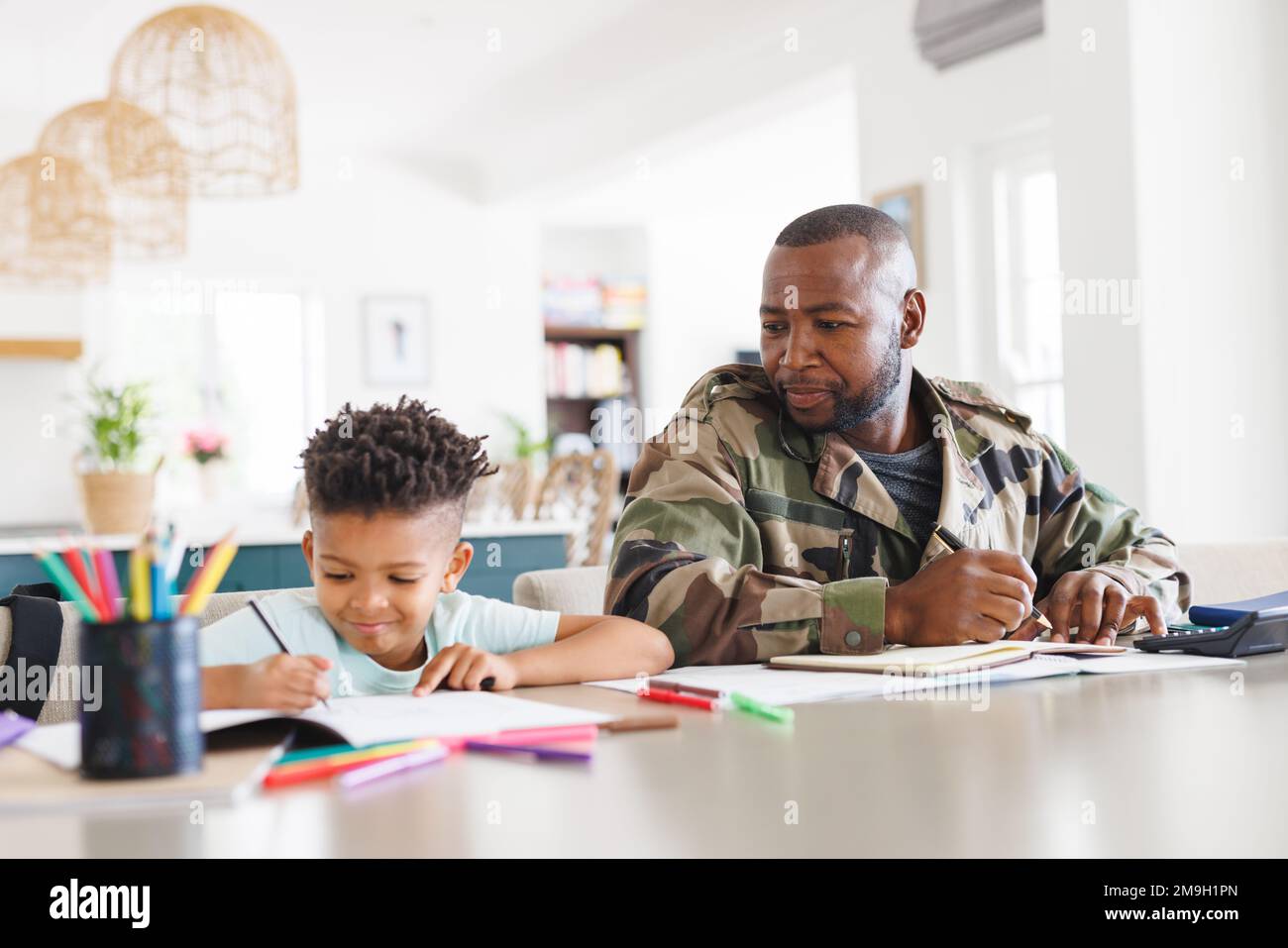 Glücklicher afroamerikanischer Vater in Militäruniform und sein Sohn arbeitet und macht Hausaufgaben Stockfoto