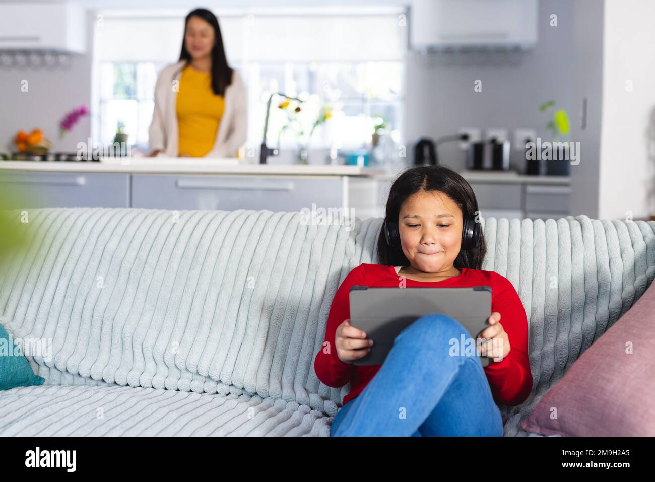 Glückliches asiatisches Mädchen, das auf dem Sofa im Wohnzimmer sitzt und ein Tablet benutzt Stockfoto