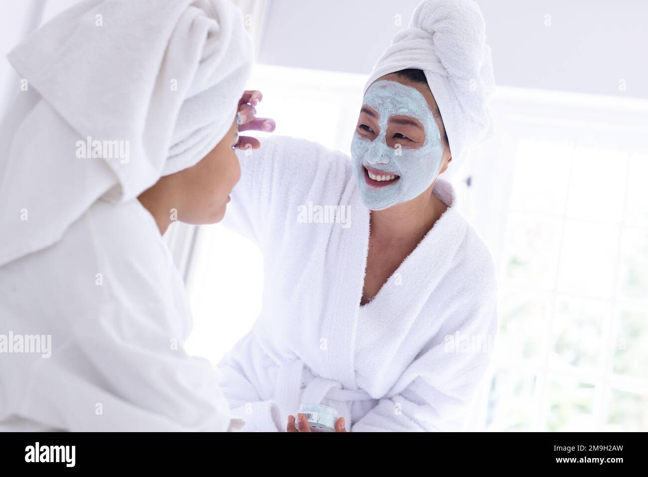 Glückliche asiatische Mutter und Tochter, die Schönheitsmasken auftragen Stockfoto