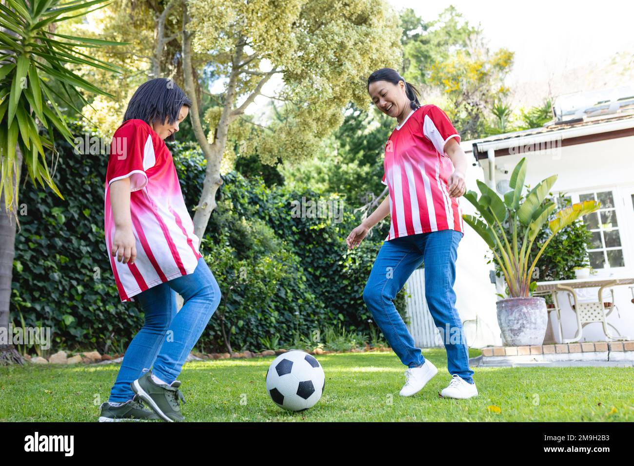 Glückliche asiatische Mutter und Tochter, die zusammen im Garten Fußball spielen Stockfoto