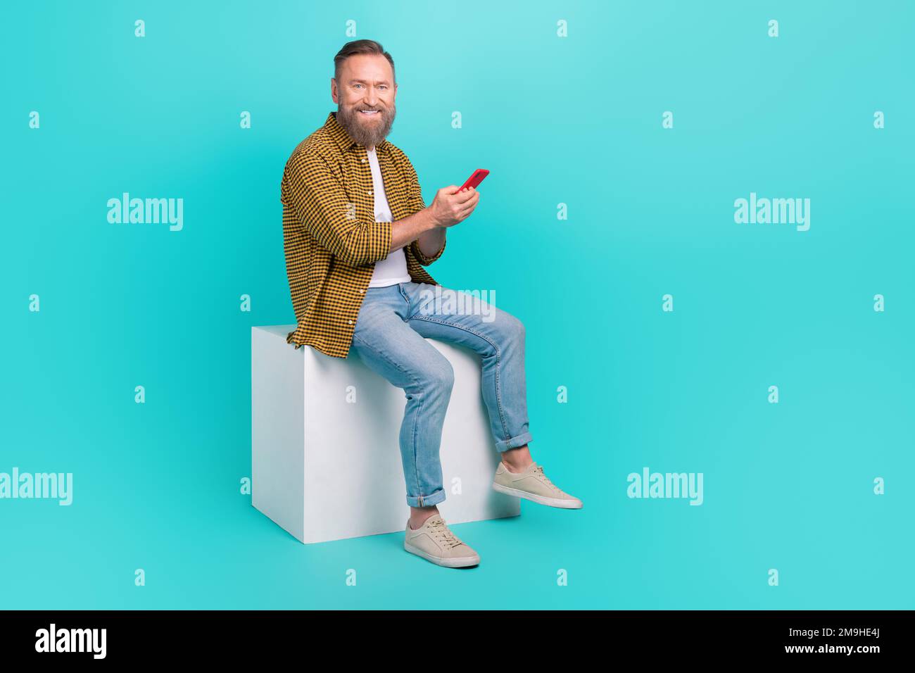 Foto eines positiven erfolgreichen Mannes Tragen trendige Kleidung Sitzen Podium Verwenden Sie moderne Gerätetechnologie isoliert auf cyanfarbenem Hintergrund Stockfoto
