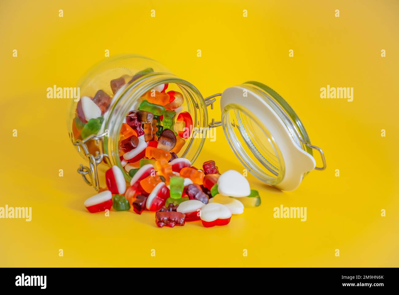 Süße Süßigkeiten Glasbehälter geöffnet mit süßen Süßigkeiten gegossen auf gelbem Tisch isoliert Stockfoto