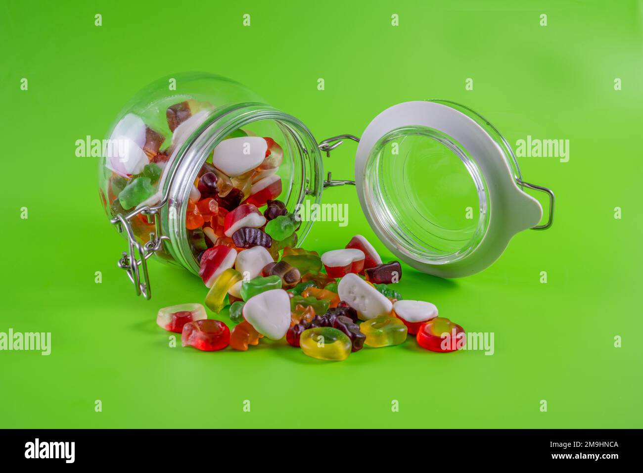 Süßigkeiten-Becher offen, Inhalt fällt auf grünen Tischhintergrund isoliert heraus Stockfoto