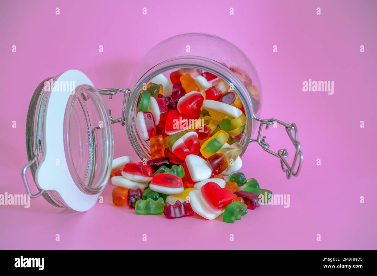 Offenes, luftdichtes Süßigkeitenglas, dessen Inhalt auf den pinkfarbenen Hintergrund ausläuft, isoliert Stockfoto