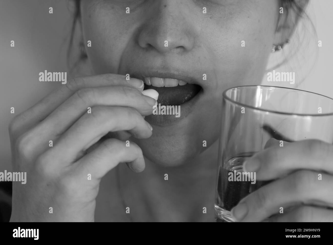 Bild einer Frau, die eine Tablette in den Mund nimmt, während sie ein Glas Wasser in der anderen Hand hält. Nebenwirkungen von Psychopharmaka und Variou Stockfoto