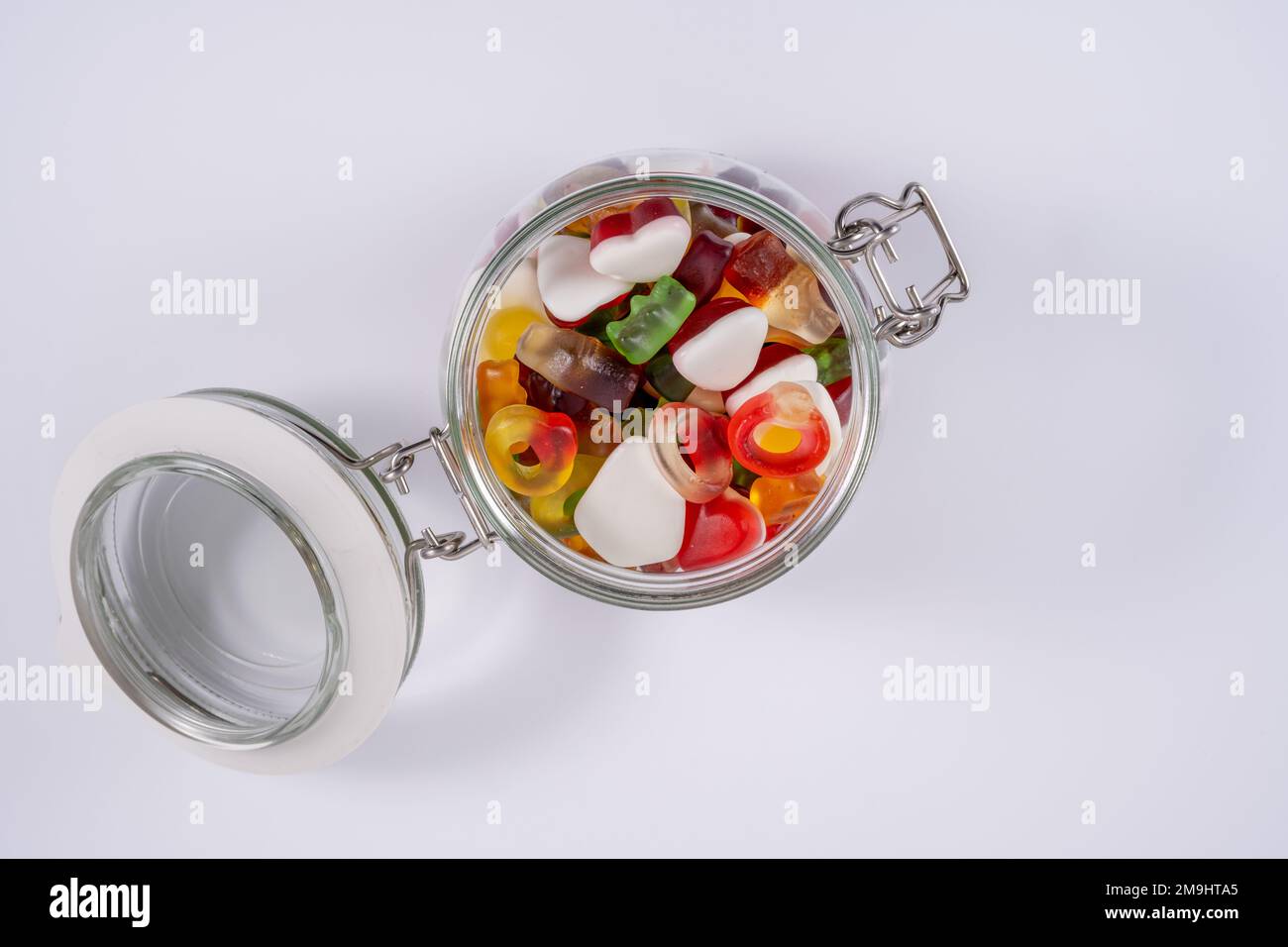 Flach liegender Blick von oben auf ein geöffnetes Süßigkeitenglas mit Süßigkeiten, isoliert auf weißem Hintergrund Stockfoto