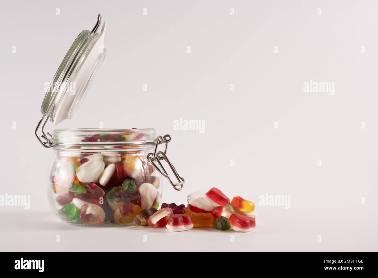 Glas-Süßigkeiten-Becher mit versiegeltem Deckel auf einem weißen Tisch, mit Süßigkeiten mit Fruchtgeschmack isoliert auf weißem Hintergrund Stockfoto