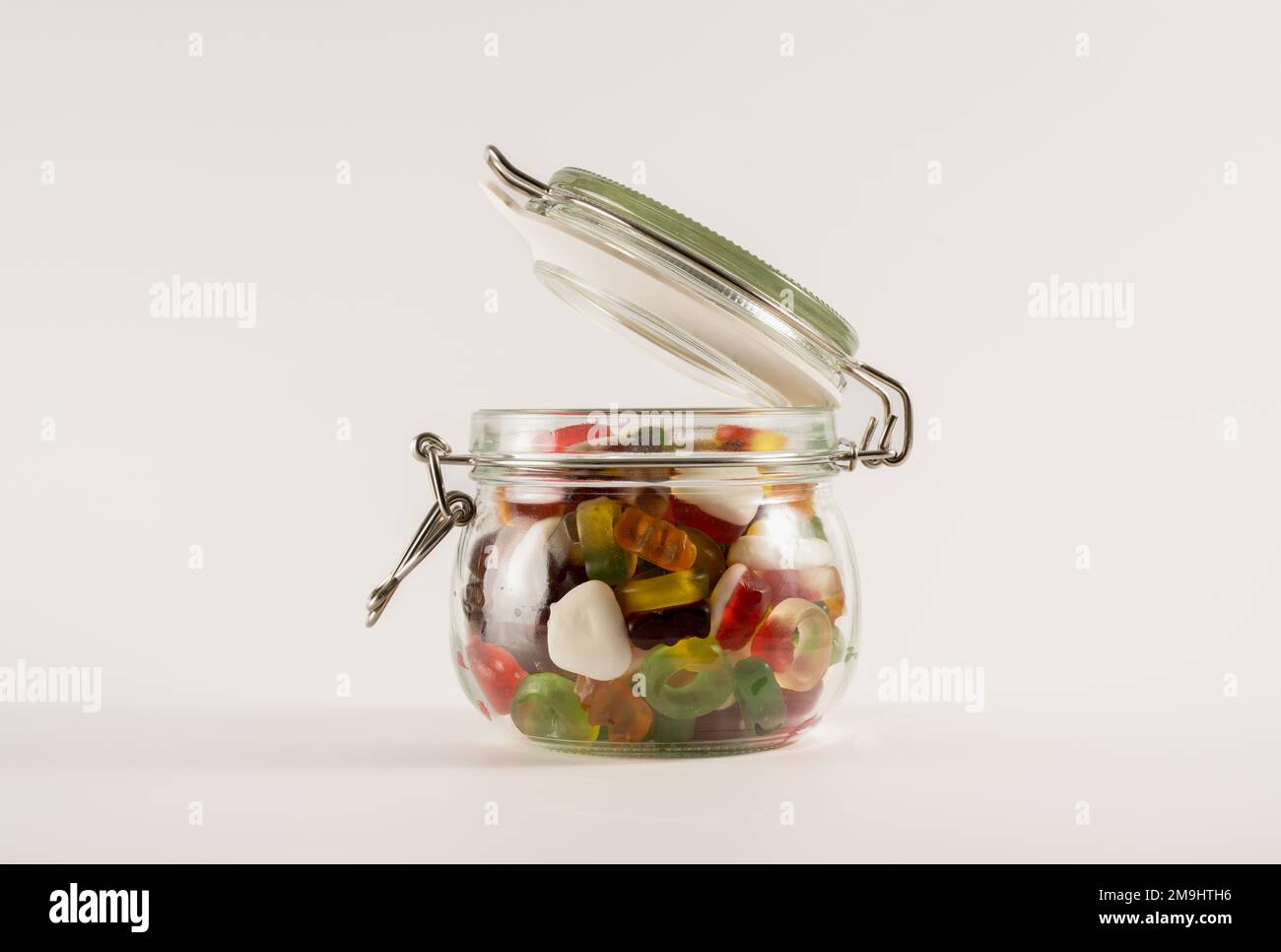 Glasbehälter mit Süßigkeiten mit Fruchtgeschmack und offenem Deckel, isoliert auf weißem Hintergrund Stockfoto