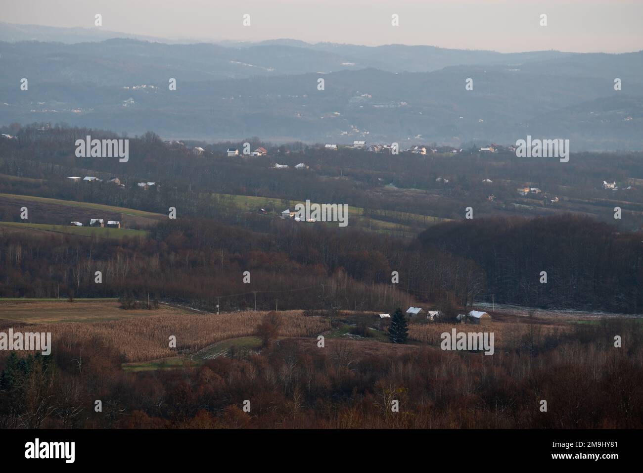 Friedliches hügeliges Dorfpanorama in der Dämmerung, erster Schnee auf den Dächern des Hauses, schöner Abend auf dem Land Stockfoto