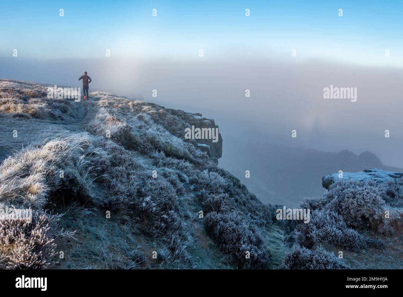 Durchbrechen des Nebels auf dem Ilkley Moor an einem kalten Tag mit dickem Frost auf der Heidekraut. Ein Läufer rennt auf dem Ilkley Moor mit dem Mond hoch Stockfoto