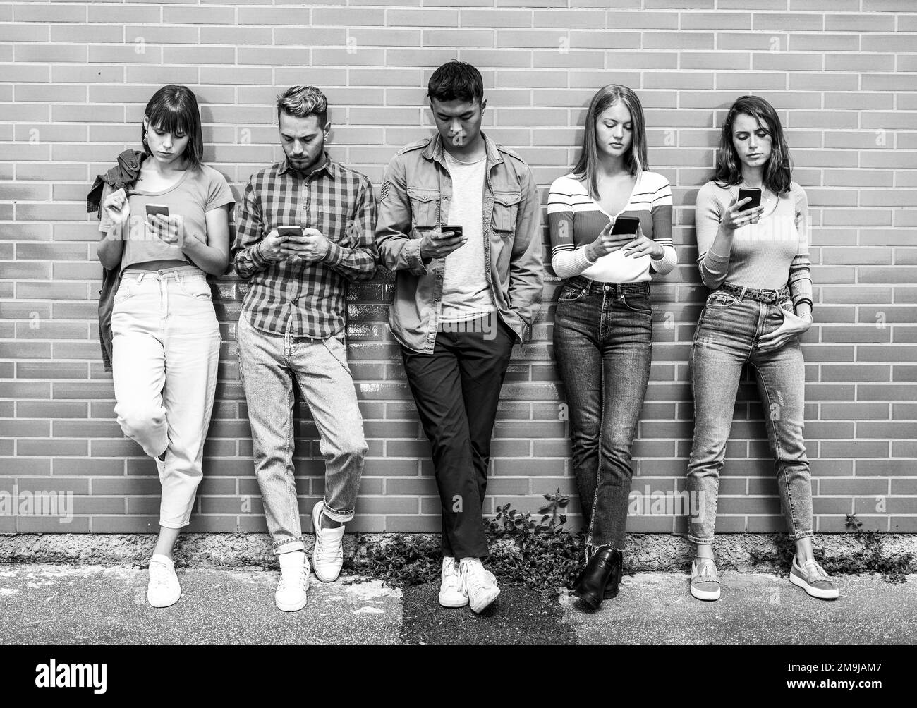 Multikulturelle Personengruppe, die ihr Smartphone im Hinterhof einer Universität verwendet - Gen z apathische Freunde, die von einem Smartphone abhängig sind - Schwarz und Weiß e Stockfoto