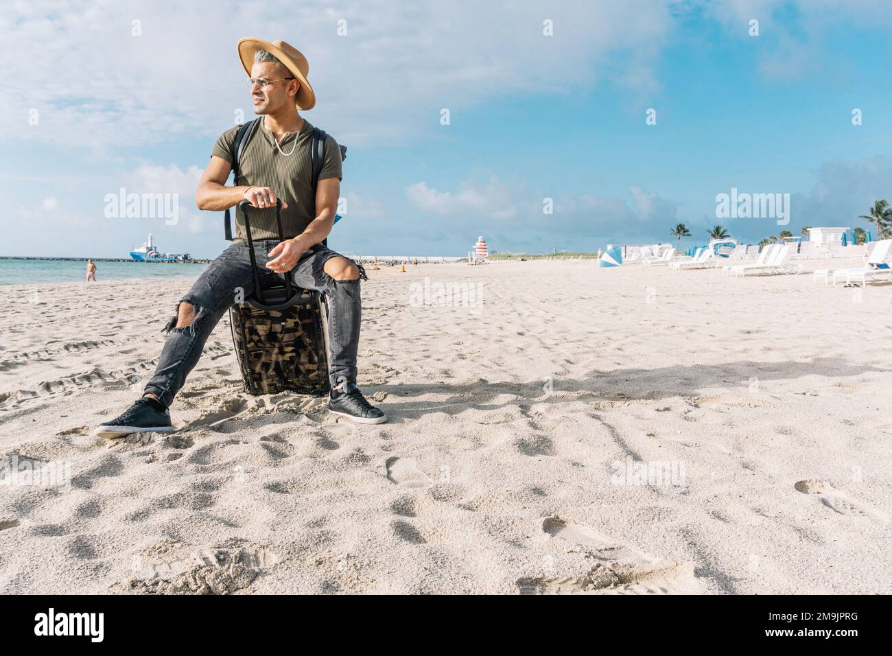 Gut aussehend und fit Kerl posiert mit einem kleinen Koffer. Ein Mann am Strand, der das Meer betrachtet. Reisekonzept Stockfoto