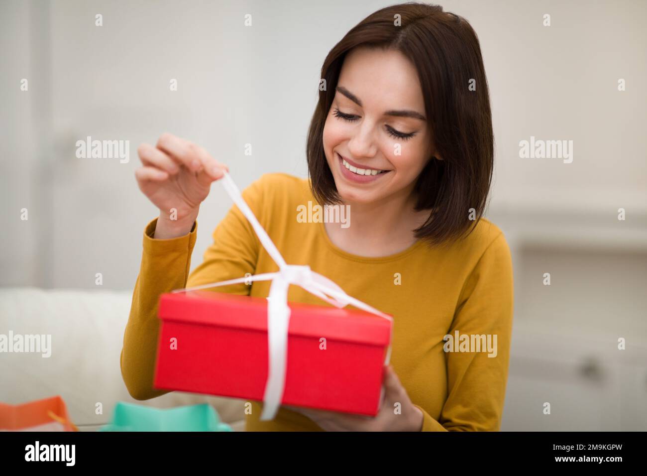 Glückliche junge Frau sitzt auf der Couch und packt den Karton aus Stockfoto