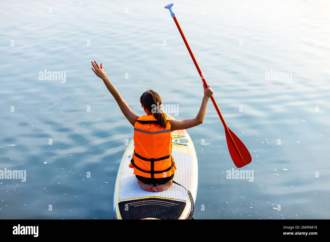 Frau in Schwimmweste sitzt am Abend am Unterbrett am Fluss, Wald im Hintergrund Stockfoto