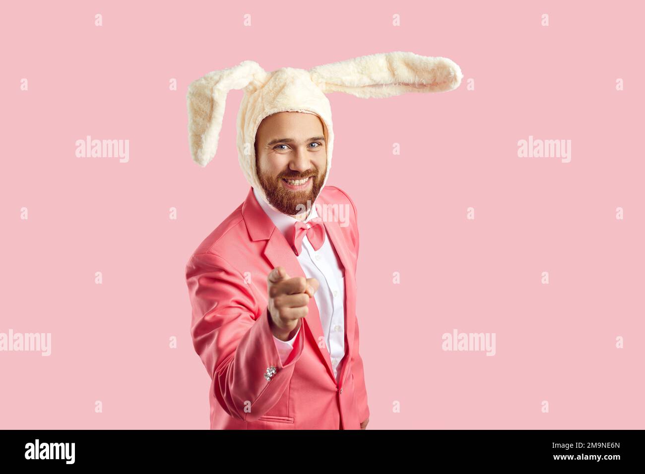 Ein glücklicher junger Mann mit lustigen Osterhäschen-Ohren, der lächelt und mit dem Finger auf die Kamera zeigt Stockfoto