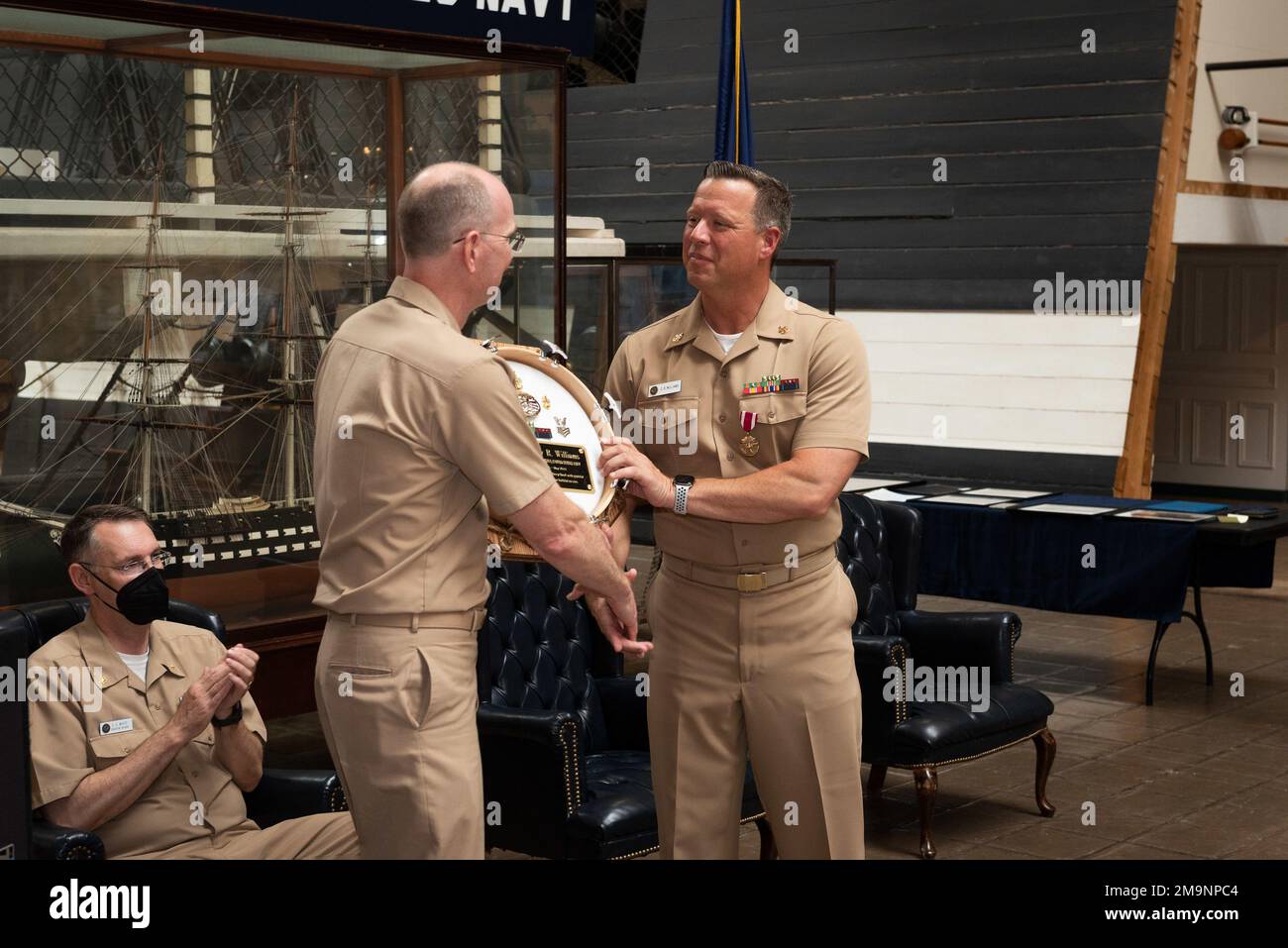 220520-N-DD694-1073 WASHINGTON (20. Mai 2022) Master Chief Musician Dave Kolo, Center, präsentiert dem Senior Chief Musician Courtney Williams bei seiner Ruhestandszeremonie eine Trommelkopfplakette. Williams, bekannt als „Stimme der Marine“ und Sprecher der letzten vier Amtseinführungen des Präsidenten, trat nach 26 Jahren in den Ruhestand. Stockfoto