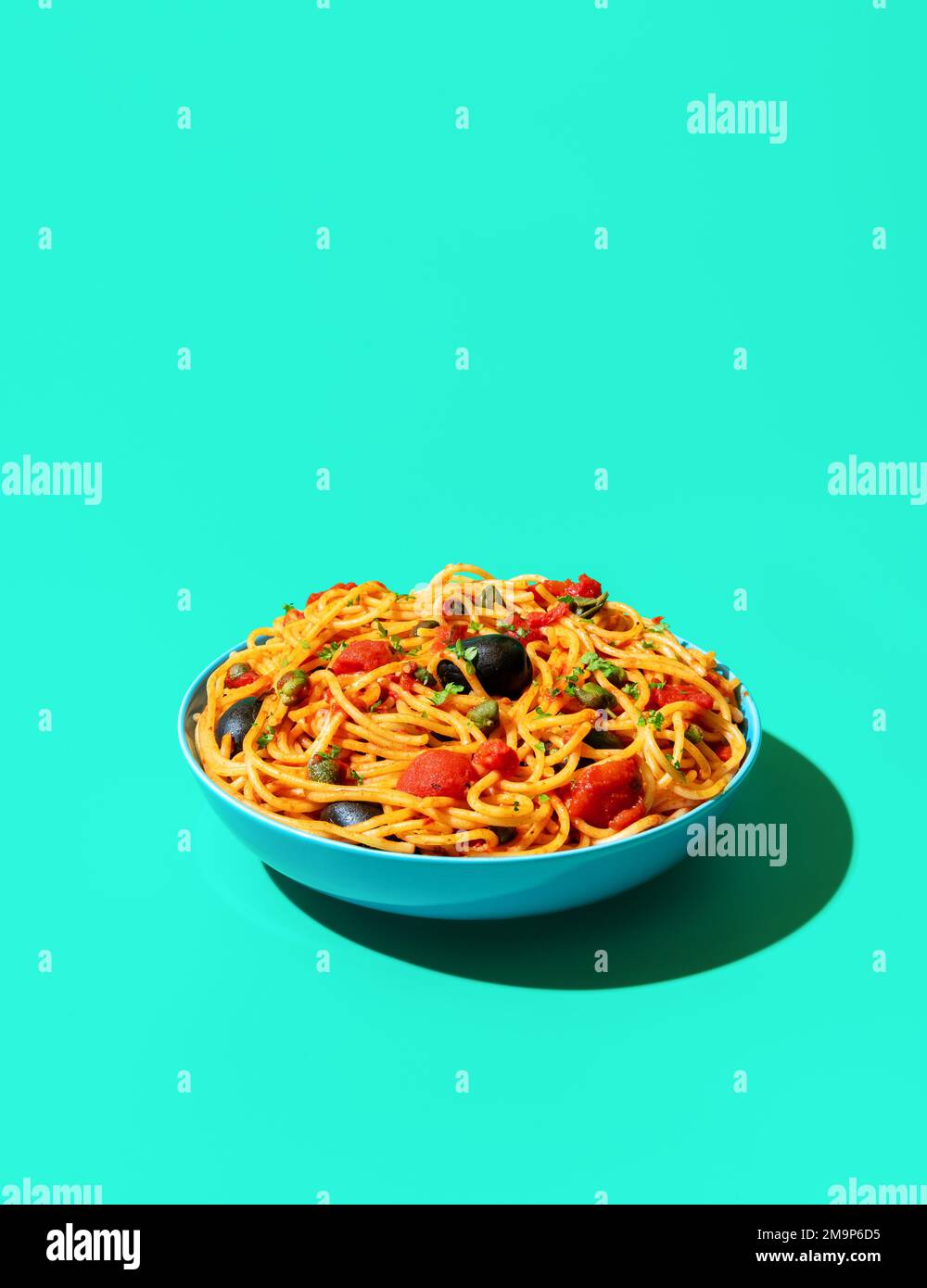 Eine Schüssel mit Pasta puttanesca minimalist auf einem grünen Tisch. veganes italienisches Gericht, Spaghetti mit Tomatensoße, schwarze Oliven und Kapern. Stockfoto