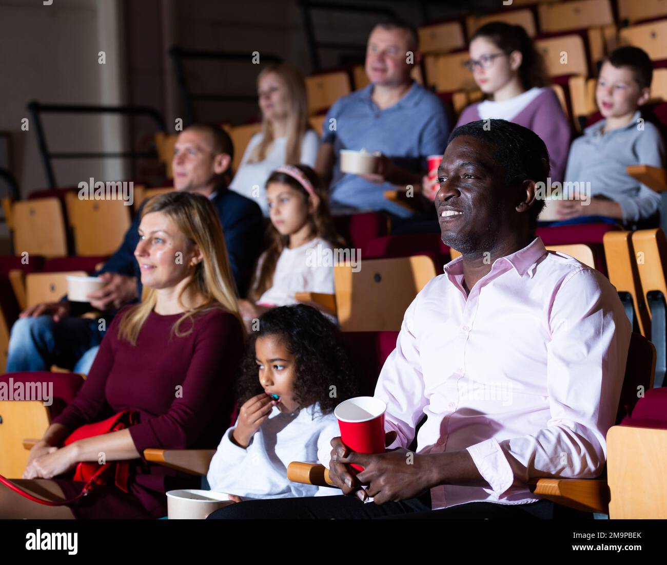 Internationale Familien essen Popcorn und sehen sich Comedy im Kinosaal an Stockfoto