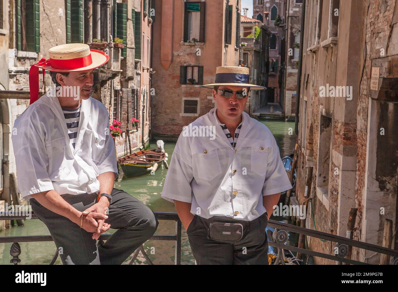 Zwei Gondoliere, gekleidet in der traditionellen Uniform eines Gondoliers, machen Mittagspause auf einer Brücke über einem Kanal in Venedig, Italien. Stockfoto