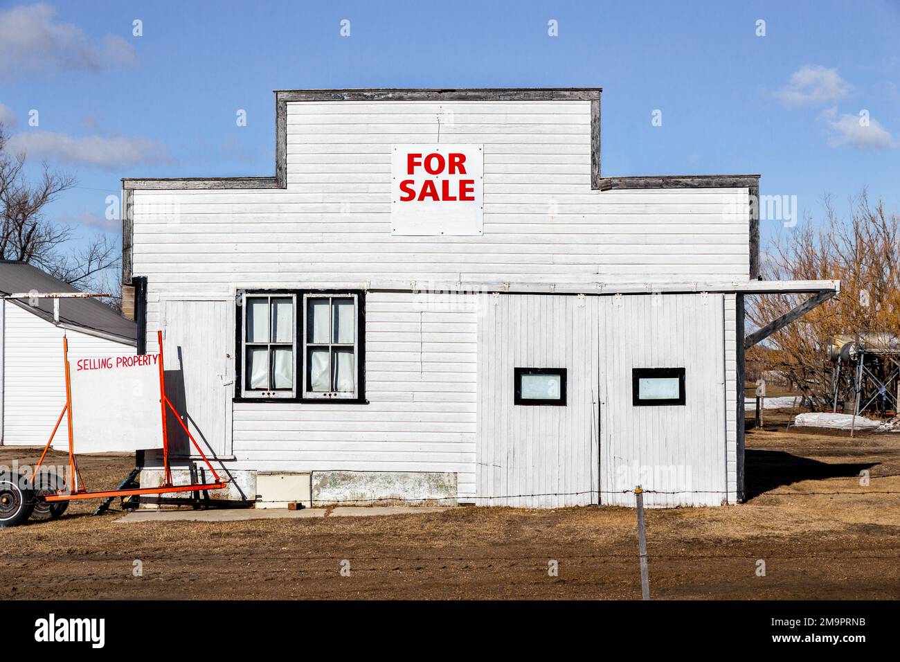 Eine alte Garage mit weißer Seitenwand und einem „zu verkaufen“-Schild entlang einer schlammigen Straße Stockfoto