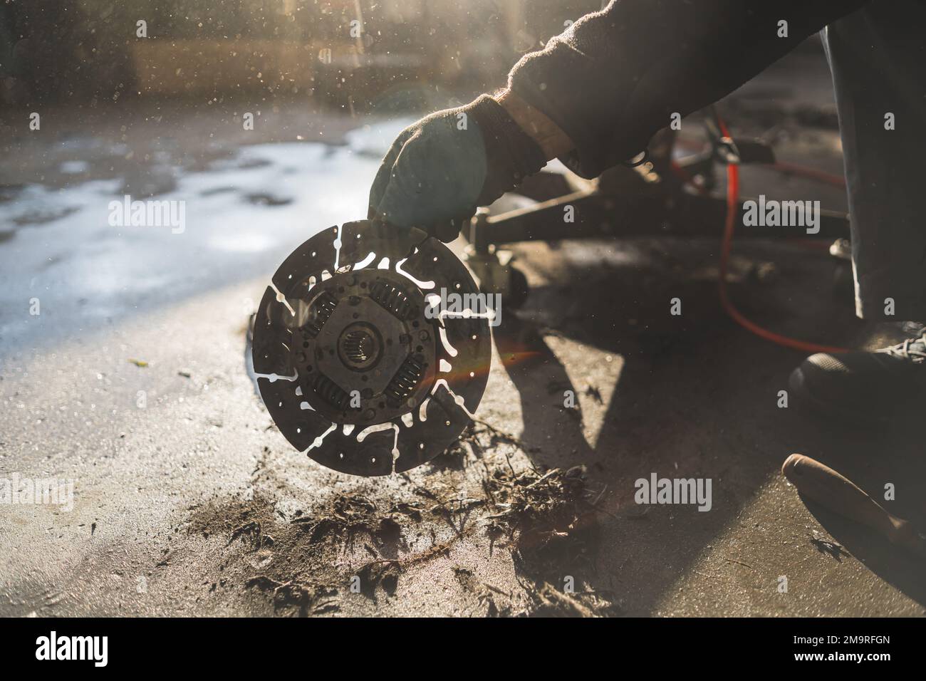 Die Hände eines Mechanikers, der eine kaputte alte silbergraue Kupplung in einer Autowerkstatt hält. Hochwertiges Foto Stockfoto
