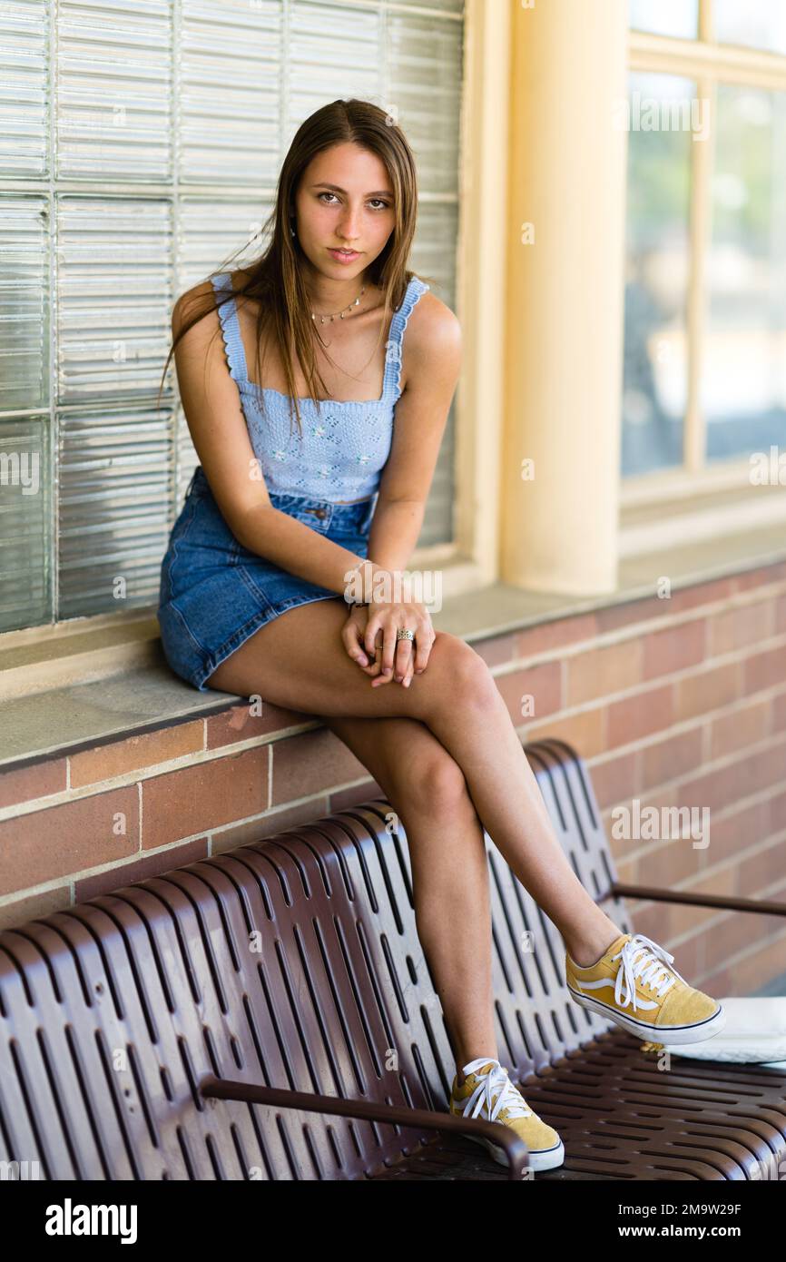 Ganzkörper-Porträt eines modischen Teenager-Mädchens, das mit den Füßen auf der Bank an einem Bahnhof sitzt Stockfoto