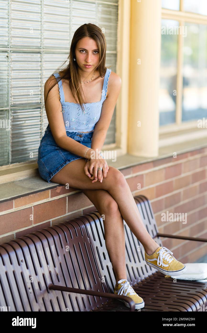 Ganzkörper-Porträt eines modischen Teenager-Mädchens, das mit den Füßen auf der Bank an einem Bahnhof sitzt Stockfoto