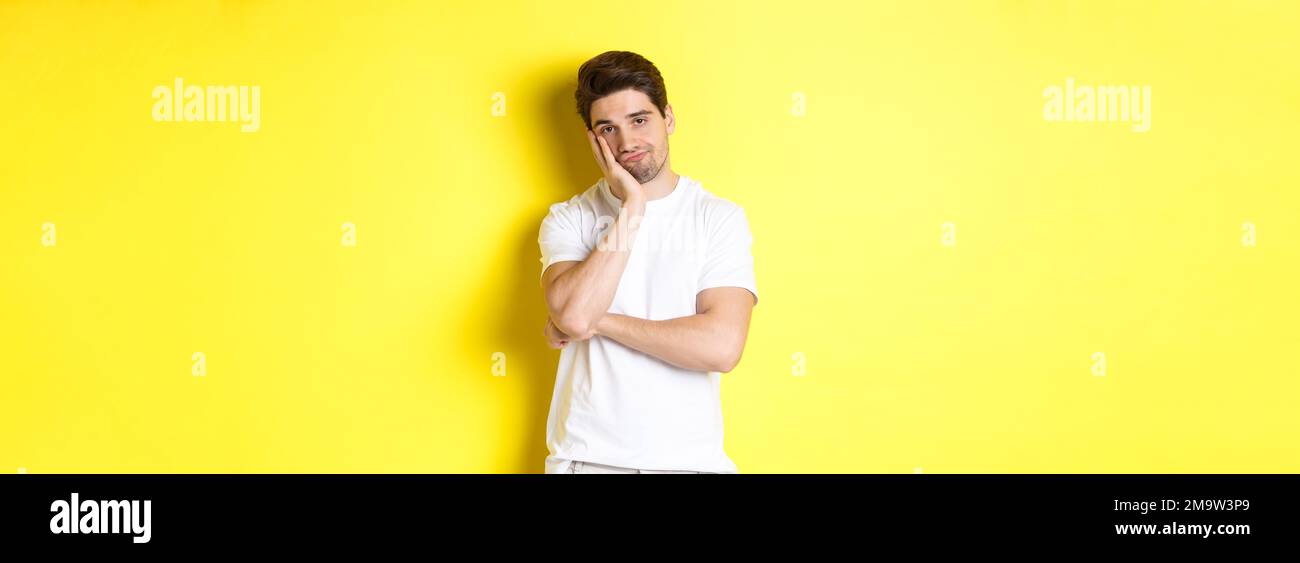 Gelangweilter und unamüsiert Mann, der mit Gleichgültigkeit schaut, in weißen Kleidern über gelbem Hintergrund stehend Stockfoto