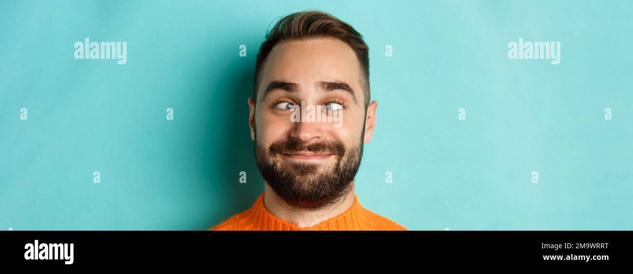 Kopfbild des lustigen kaukasischen Mannes, der Gesichter macht, schielend und lächelnd dumm, über hellblauem Hintergrund stehend Stockfoto