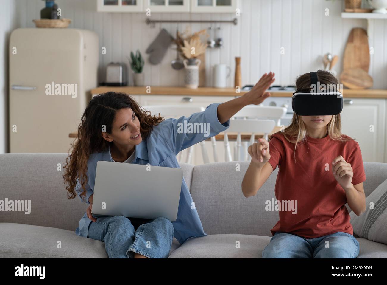 Mutter schaut Tochter Tochter Tochter an und erforscht virtuelle Realität als Zuhause. Familien und neue Technologien Stockfoto
