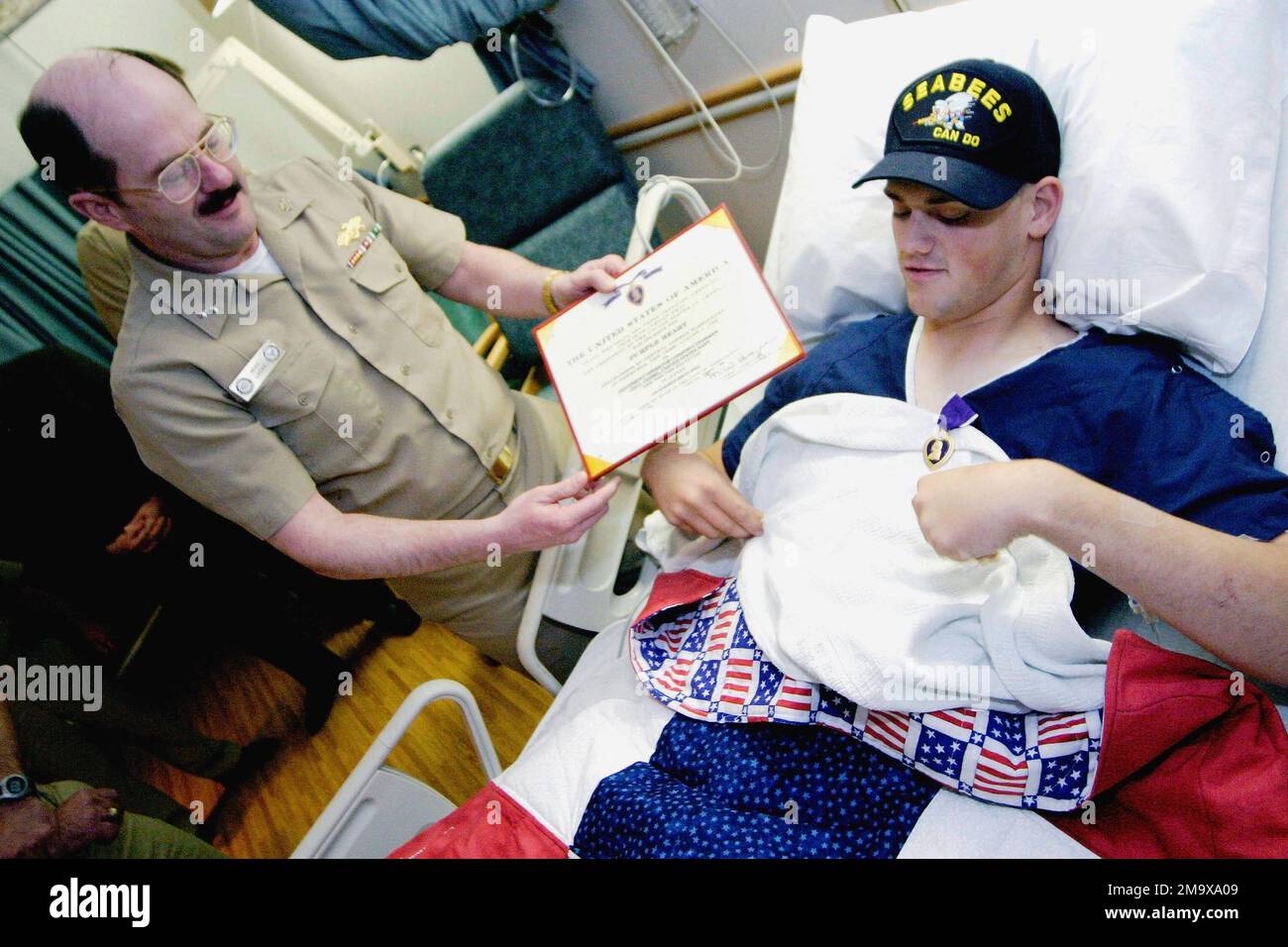 US Navy (USN) Konteradmiral (RADM) Michael K. Loose, Commander, Naval Facilities Engineering Command und CHIEF of Civil Engineers, überreicht die Purple Heart Medaille dem USN-SEEMANN Leo 'Jerry' Geibel, Equipment Operator Constructionman. SN Geibel, Naval Mobile Construction Battalion Seven Four (NMCB-74), Gulfport, Mississippi (MS), erlitt schwere Verletzungen an seinen Beinen, als sie während der Operation IRAQI FREEDOM eine Raketengranate (RPG) ablenkten, die an einer Wand hinter ihm im Ramadi-Gebiet im Irak explodierte. Die Navy-Ärzte von SN Geibel erwarten, dass er sich vollständig erholt. Basis: Marinemedizin Stockfoto