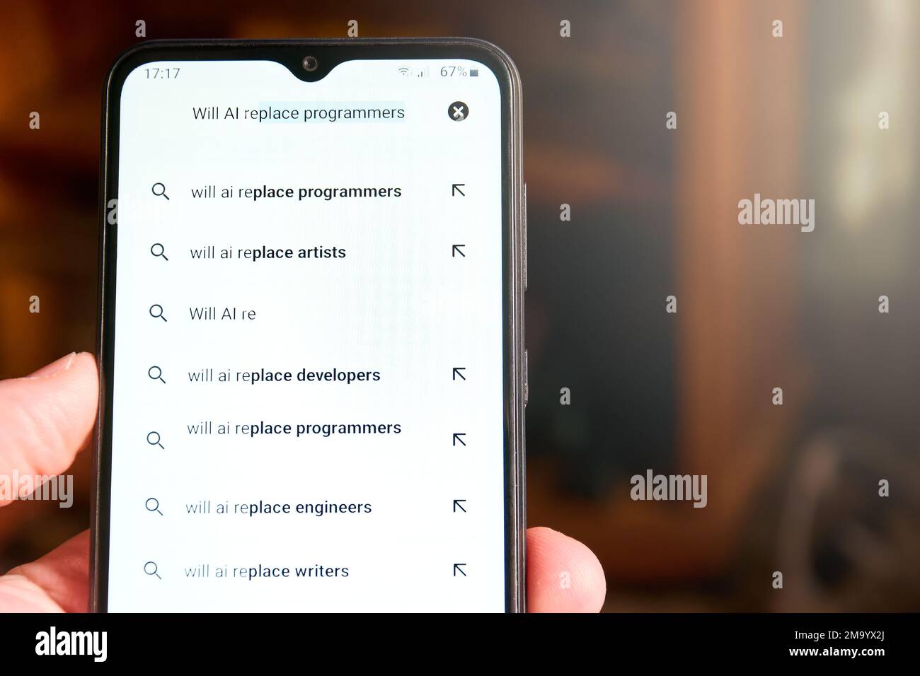 Horizontale Nahaufnahme des Mobiltelefonbildschirms mit der Suche „wird AI Programmierer ersetzen“ und einer Liste der vorgeschlagenen Suchvorgänge unten. Leute suchen nach KI, Konz Stockfoto