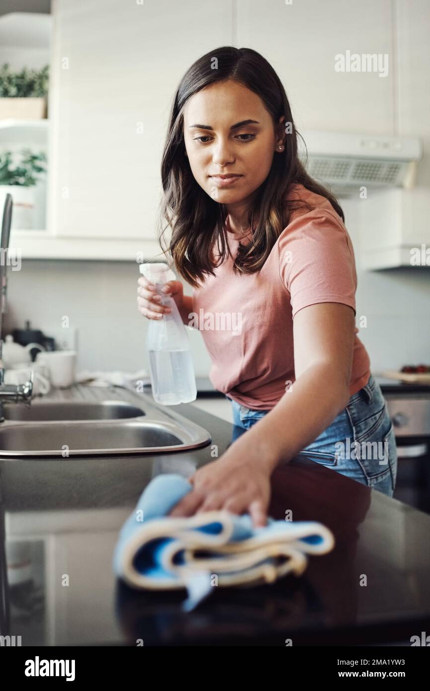 Ich putze immer diese Arbeitsflächen. Eine attraktive junge Frau, die zu Hause mit einem Tuch die Küchenablagen reinigt. Stockfoto