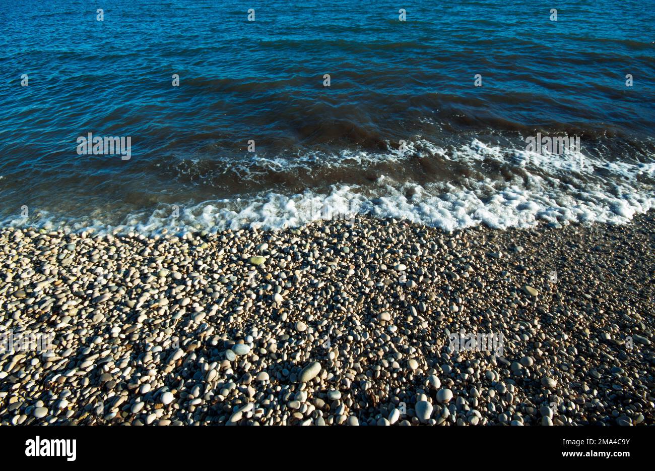 Ufer des Mittelmeers an einem der Steinstrände der Stadt White Coast Altea, in Alicante beobachten Sie, wie die Welle auf den Steinen endet. Stockfoto