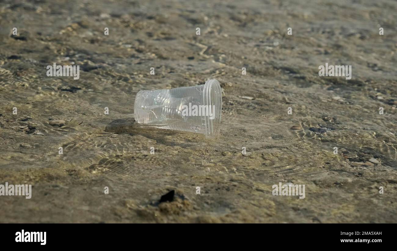 Der transparente Kunststoffbecher wird vom Wind in die Küstenzone zum Meer getragen. Plastikverschmutzung der Surfzone. Rotes Meer, Ägypten Stockfoto