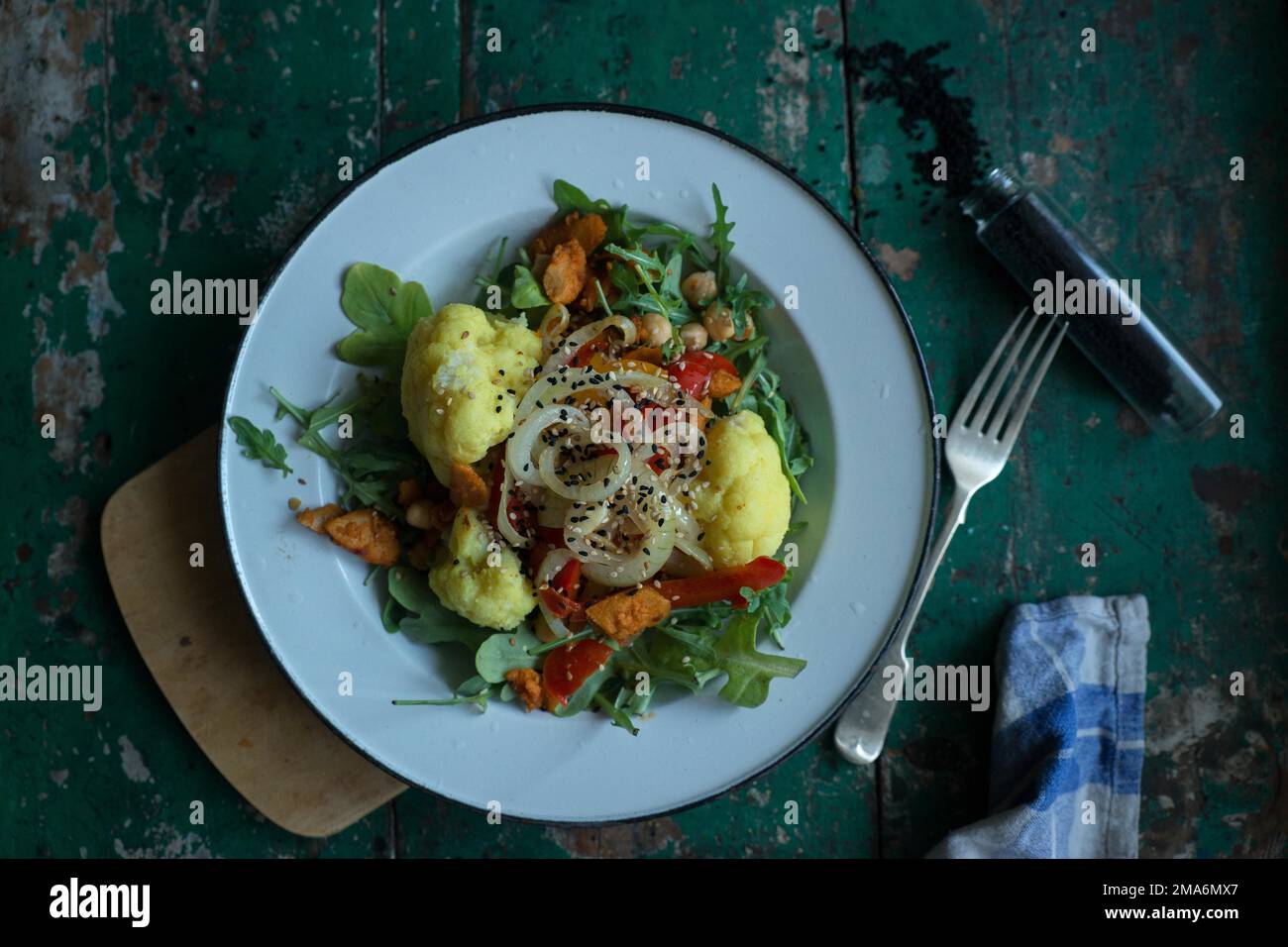 Veganer Blumenkohlsalat auf einer Blechplatte mit schwarzem Kreuzkümmel auf einem rustikalen Tisch Stockfoto