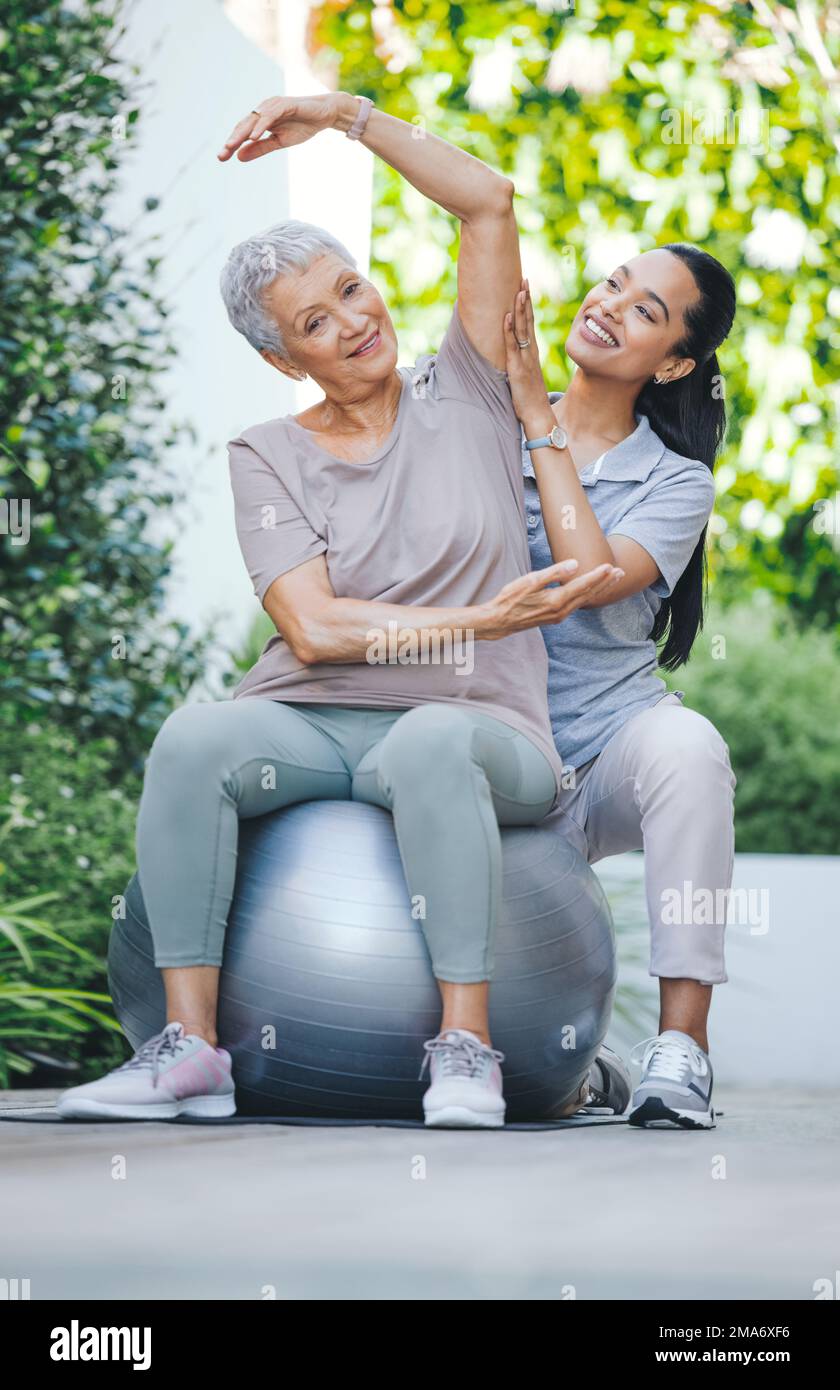 Ich hoffe nur, dass ich nicht so glücklich werde, dass ich langweilig werde. Eine ältere Frau, die während einer Sitzung mit einem Physiotherapeuten draußen einen Sportball benutzt. Stockfoto