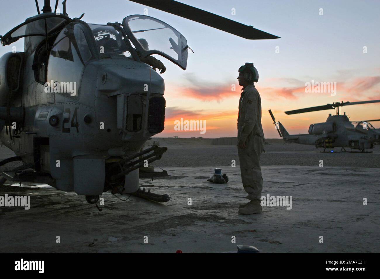 Ein Marine des US Marine Corps (USMC) steht neben einem geparkten USMC  AH-1W Super Cobra Helicopter, Marine Light Attack Helicopter Squadron 369  (HML/A-369), in Forward Operation Base (FOB) Al Qaim, Al Anbar