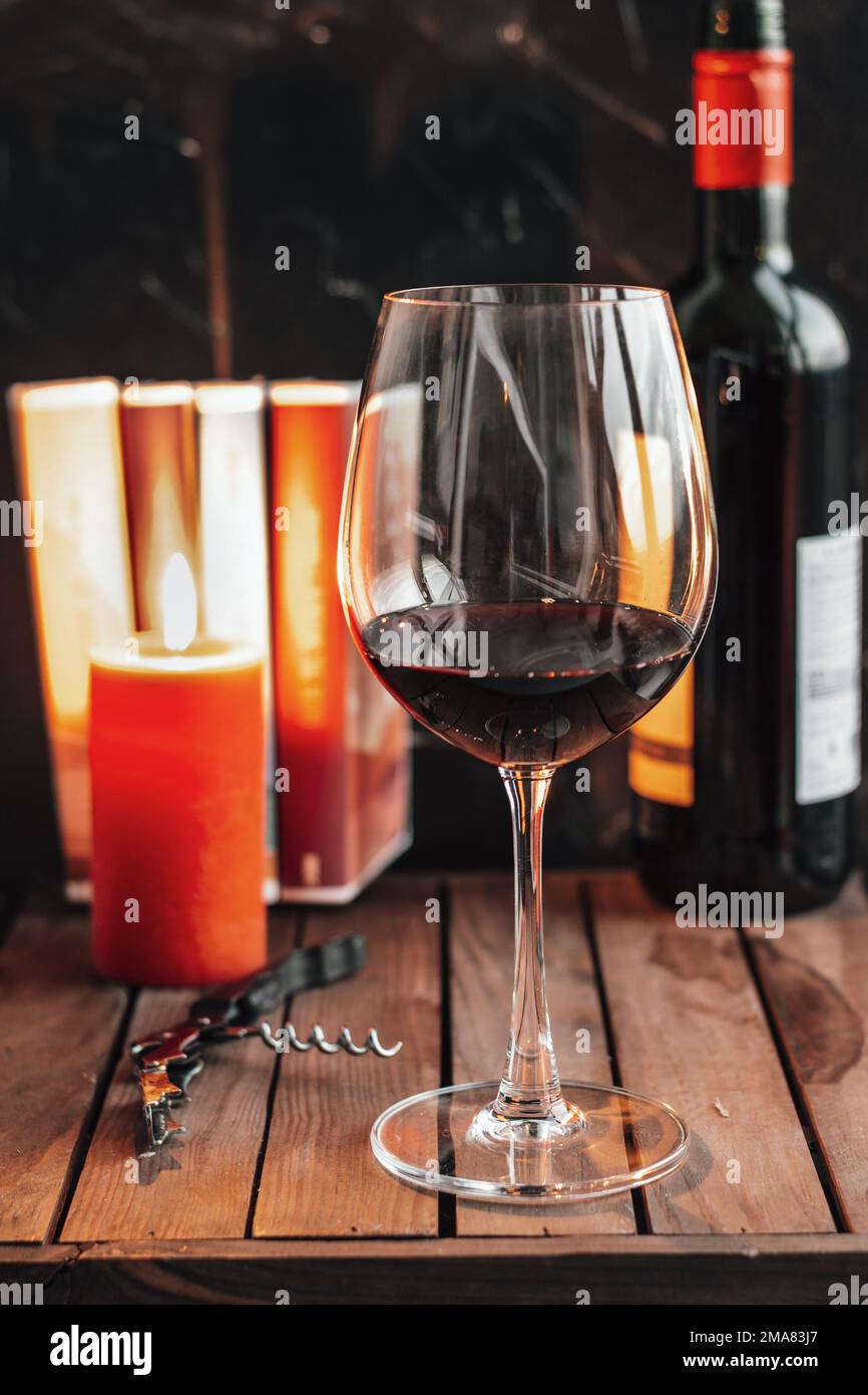 Rotwein im Glas. Ein Glas Rotwein liegt auf dem Tisch. Eine Kerze, Bücher und eine Flasche Wein auf dem Tisch Stockfoto