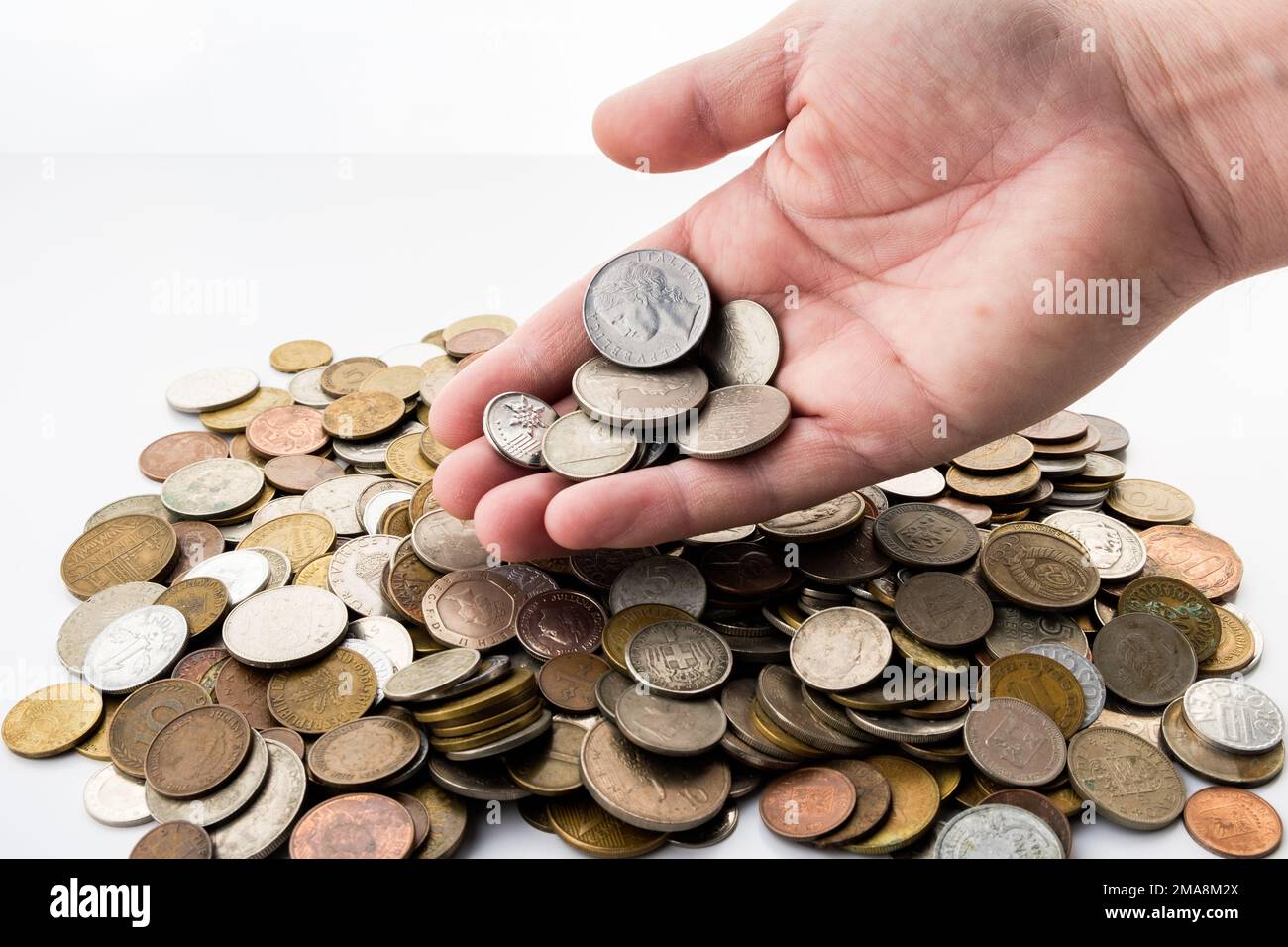 Eine Hand gießt mehr Münzen auf einen Haufen alter gebrauchter Münzen. Aktuelles Geld der Welt Stockfoto