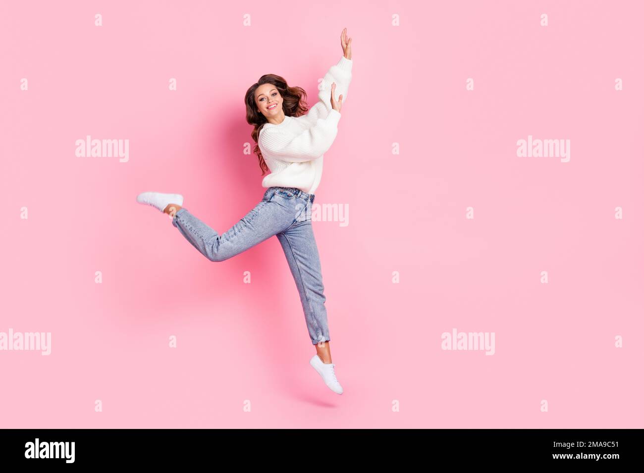 Langes Foto einer aufgeregten, glänzenden Dame mit weißem Pullover, der hoch springt und leer tanzt, isolierter pinkfarbener Hintergrund Stockfoto