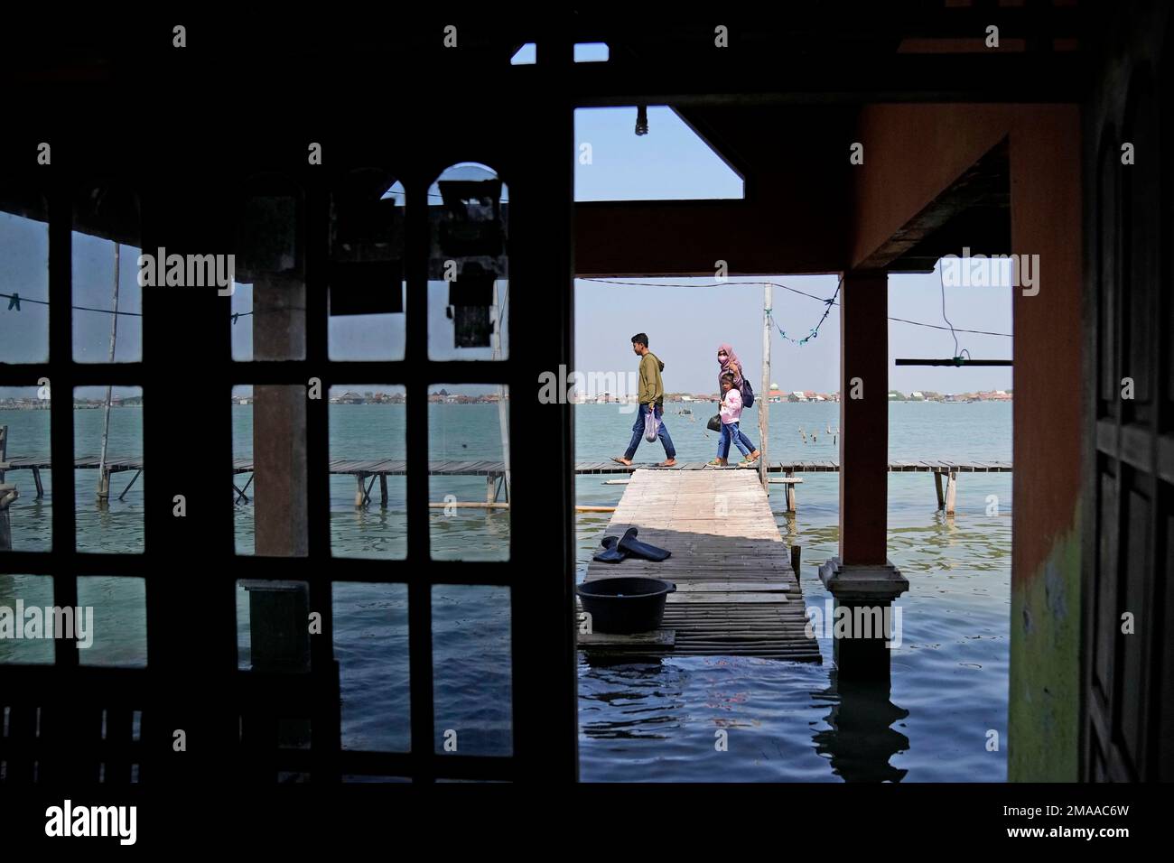 A family walks through Timbulsloko, Central Java, Indonesia, Sunday, July 31, 2022. In Timbulsloko, homes have been fortified with raised floors and dirt walkways, causing people to crouch when walking through shortened doors. (AP Photo/Dita Alangkara) Stockfoto