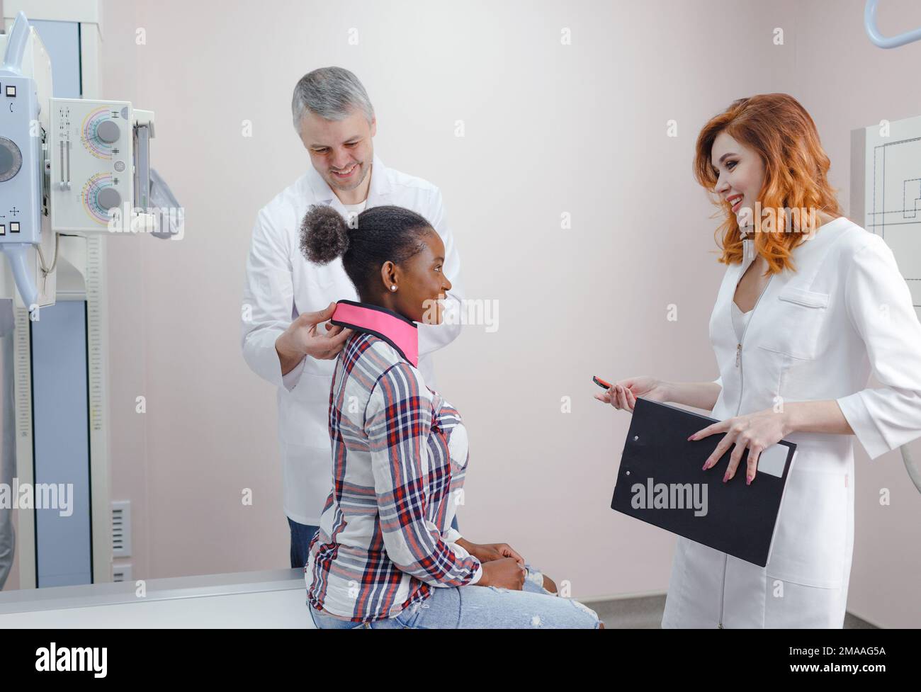 Ein Radiologe bereitet zusammen mit einer Assistentin einen afroamerikanischen Patienten auf eine Röntgenaufnahme vor Stockfoto