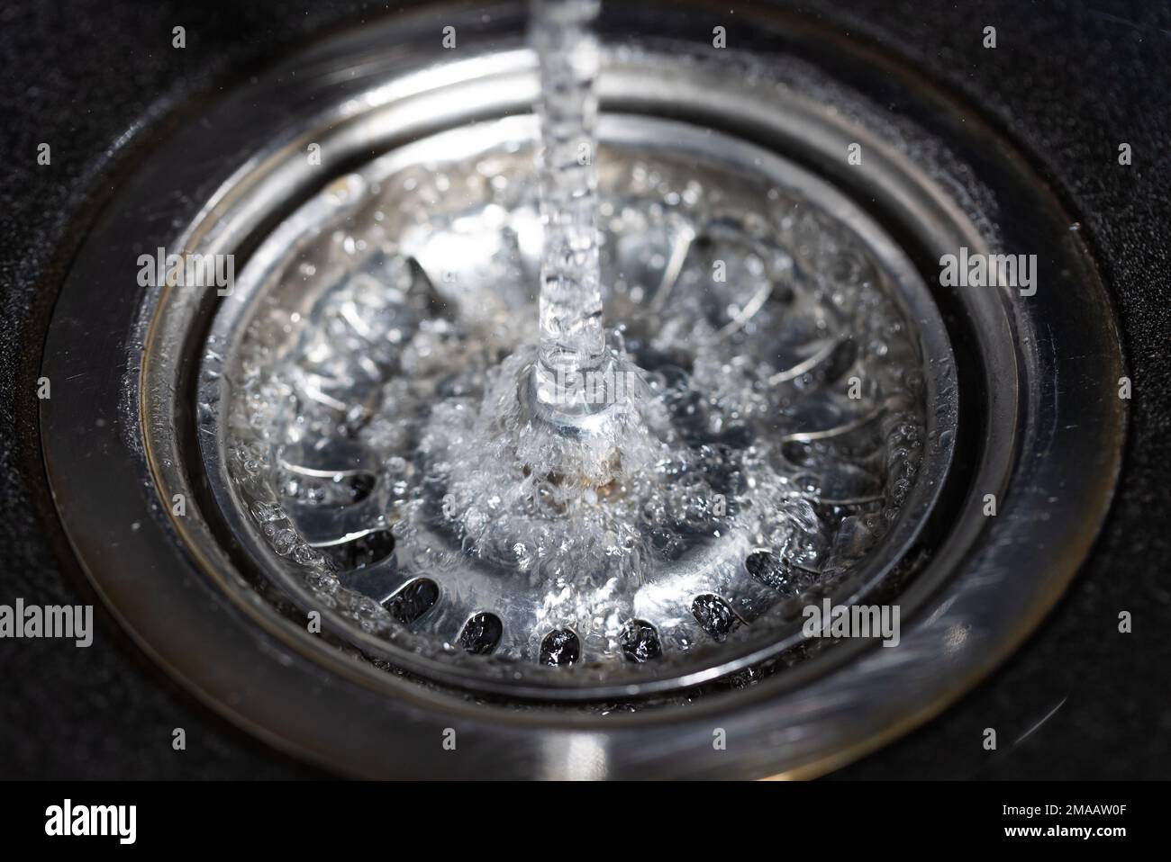 Das Wasser fällt vom Wasserhahn zum rostfreien Waschbecken und fließt hinunter zum Wasserloch, Getränkekonzept Stockfoto