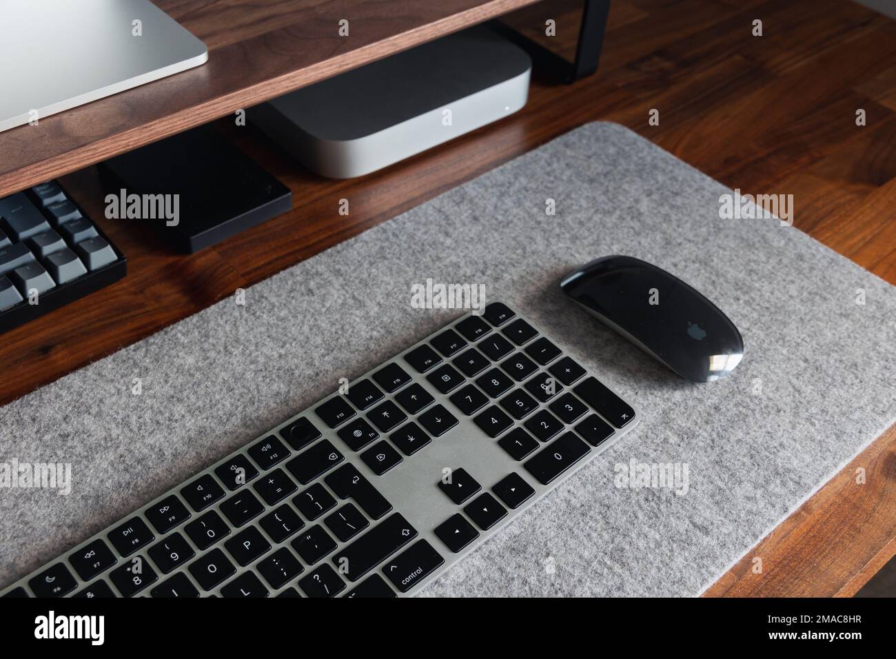 LONDON - 22. NOVEMBER 2022: Minimale Schreibtischeinrichtung mit Apple-schwarzer Tastatur und Maus auf braunem Walnussholzhintergrund Stockfoto